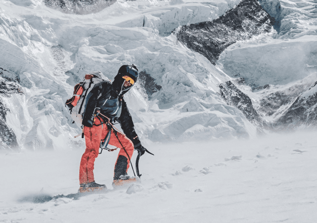 Climber in high-altitude mountain gear navigating a snowstorm in remote Himalayan terrain
