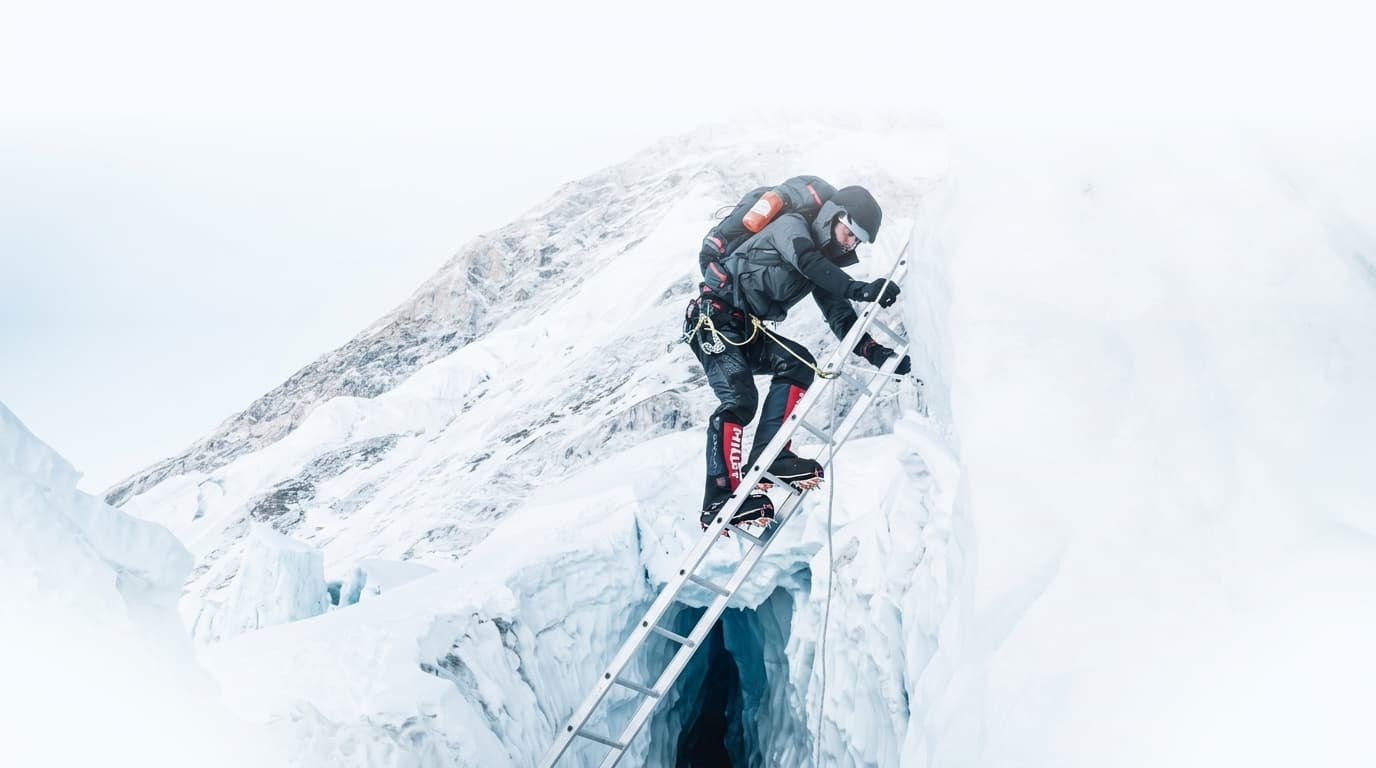 Expedition mountaineer climbing ladder over glacier crevasse